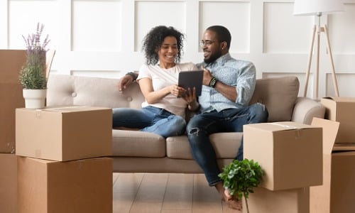 Happy couple sitting on sofa of new home using tablet  